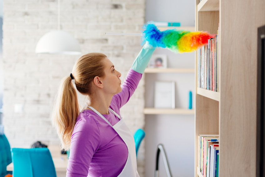 femme de ménage utilisant un plumeau multicolore pour faire la poussière dans une bibliothèque