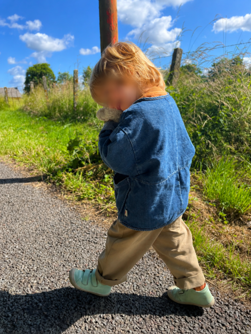 Jeune enfant marchant sur un chemin de campagne avec veste en jean et chaussures vert d’eau souples