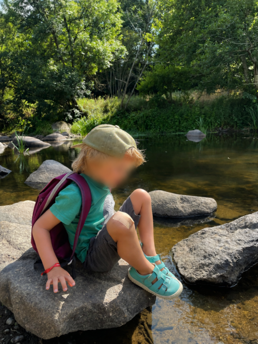 Enfant assis sur un rocher au bord d’une rivière avec chaussures turquoise souples