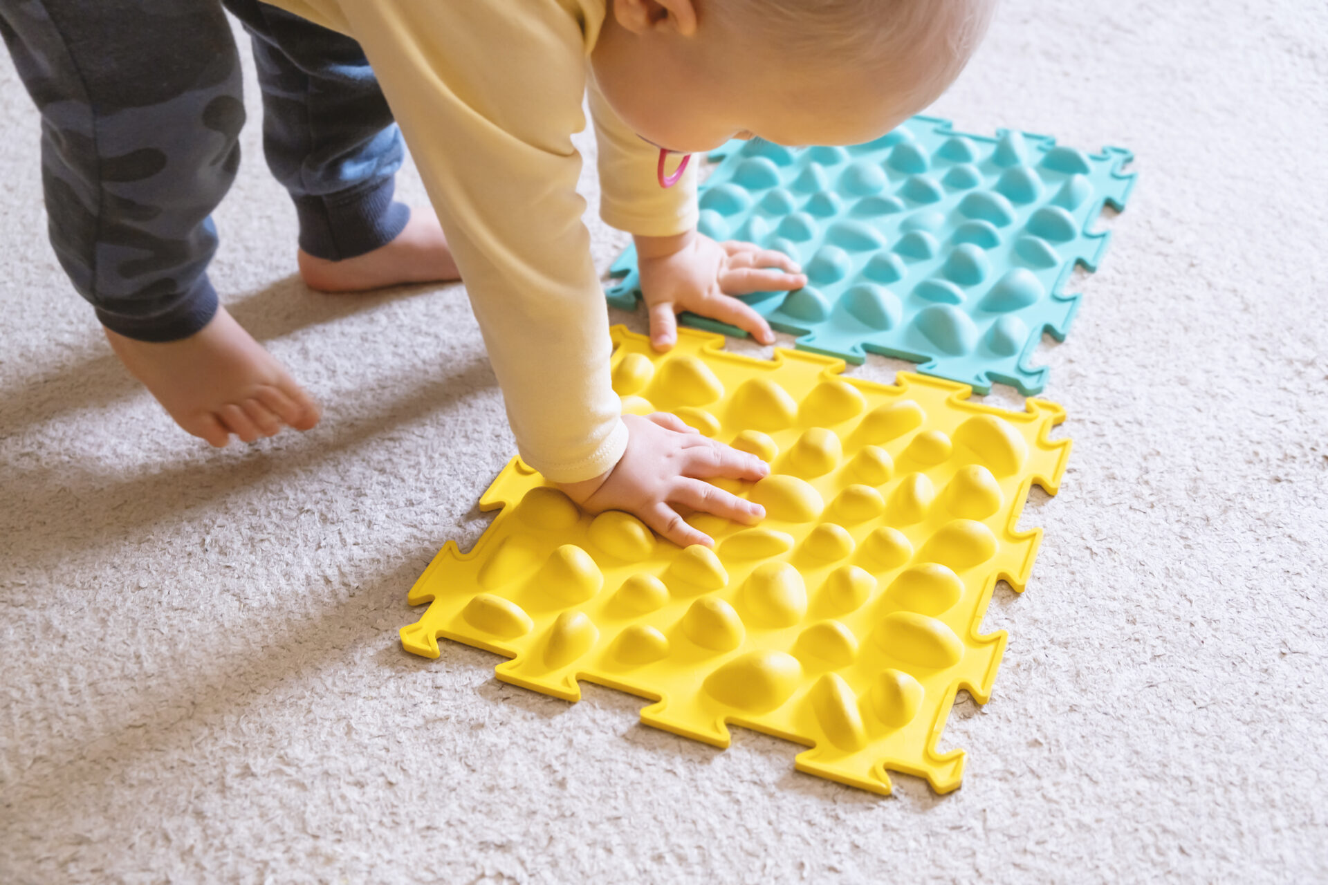 Bébé explorant des tapis sensoriels colorés pour développer la motricité et la perception tactile.