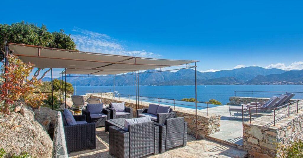 Terrasse d’une villa de luxe en Corse avec salon extérieur et vue panoramique sur la mer et les montagnes corses.